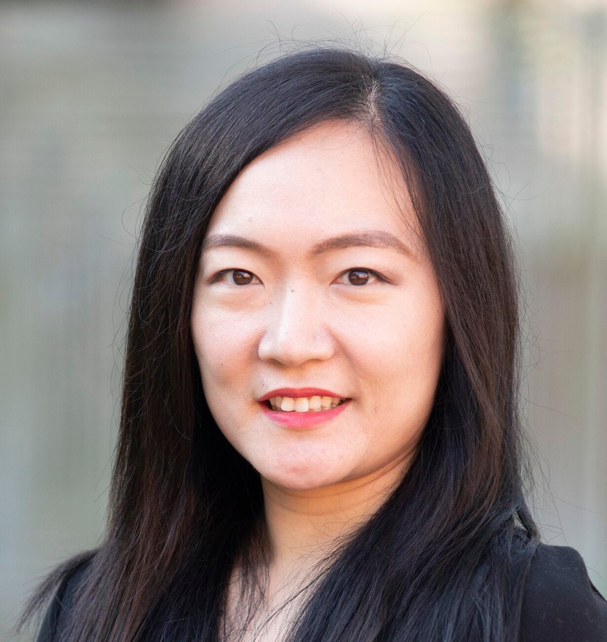 Tingyu Zhou smiling, with long black hair and red lipstick, wearing a black top.